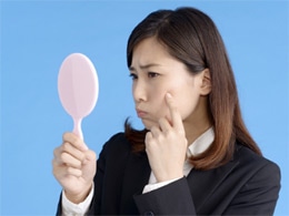 鏡を見ながらニキビを気にしている女性
